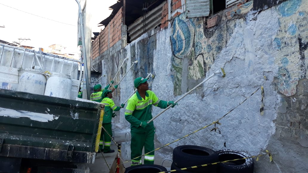 Três funcionários da Subprefeitura Ipiranga estão pintando de branco um muro
